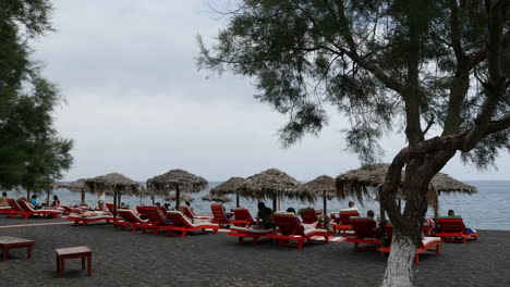 Greece-Santorini-Perissa-Tourists-Relaxing-On-Black-Sand-Beach
